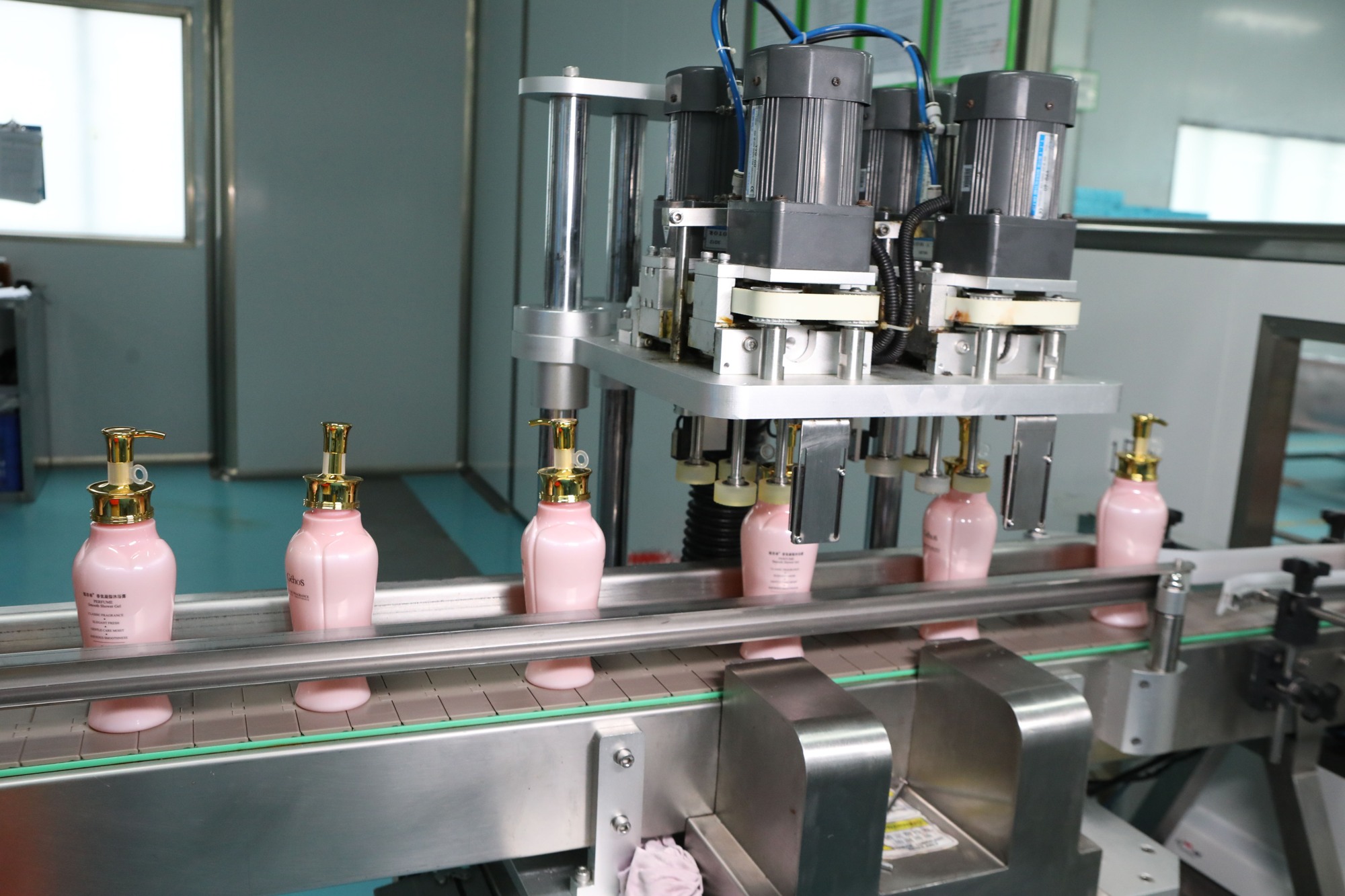 Pink cosmetic bottles with gold pumps moving through an automated capping line